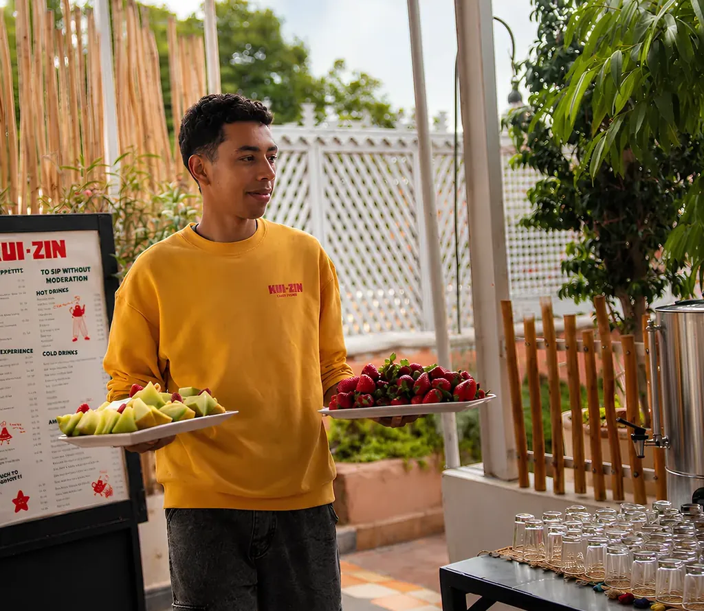 Un serveur de Kui-Zin portant un plateau de fruits frais, devant l'ardoise du restaurant
