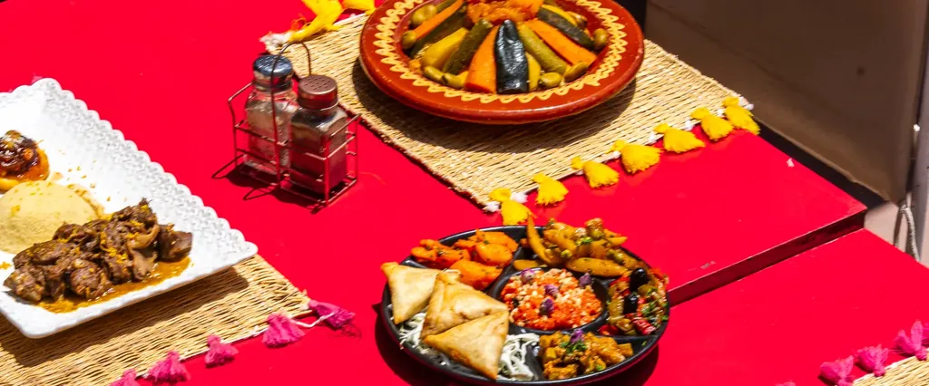 Tables rouges dressees pour le diner sur la terrasse, tajines et sets en paille